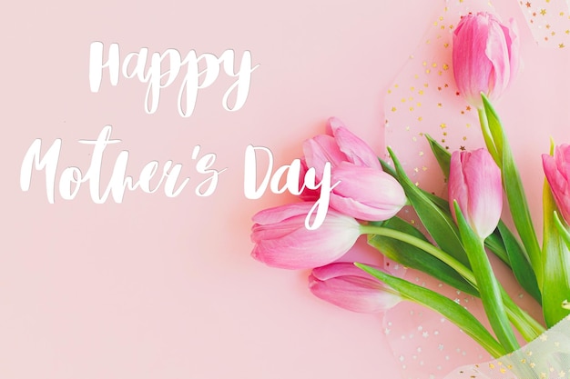 Happy mothers day text on pink tulips bouquet on pink\
background stylish greeting card happy mother\'s day gratitude and\
love to mom handwritten lettering