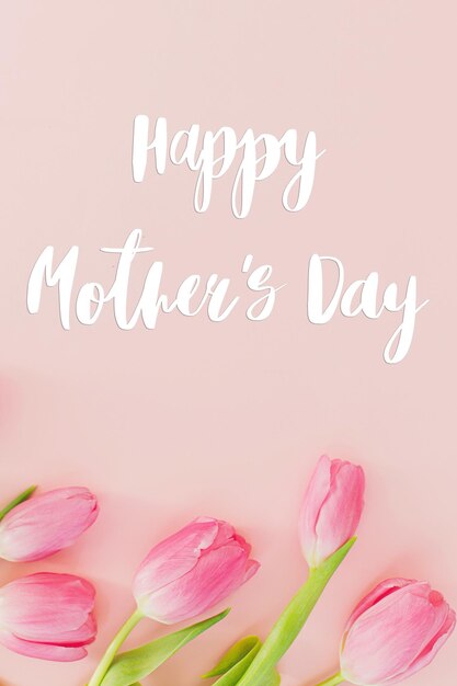 Happy mothers day text on pink tulips flat lay on pink background Stylish greeting card Happy Mother's Day gratitude and love to mom Handwritten lettering