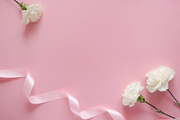 Happy Mothers day. White flower with ribbon on a pink pastel background with copyspace top view