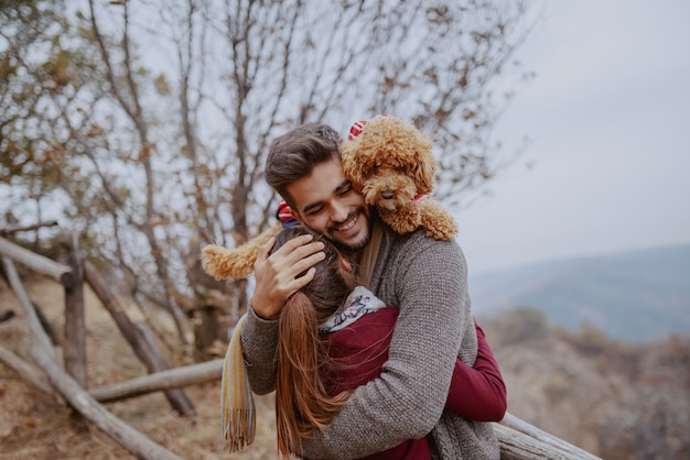 Счастливая многокультурная влюбленная пара одела случайные объятия в природе на осень. Человек, имеющий свою собаку на плечи.