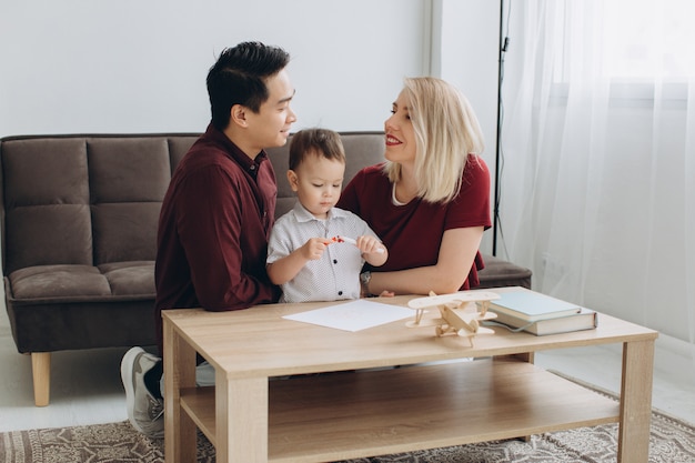 Happy multicultural family. Asian man and Caucasian woman drawing with their son.