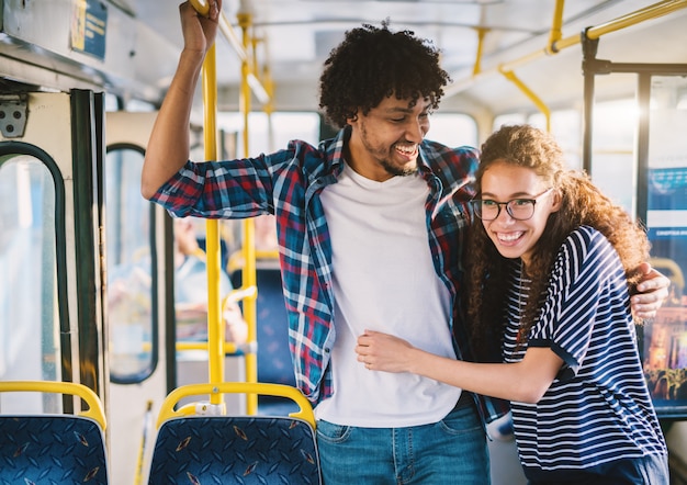 バスでバーを保持している幸せな多文化の若いカップル。