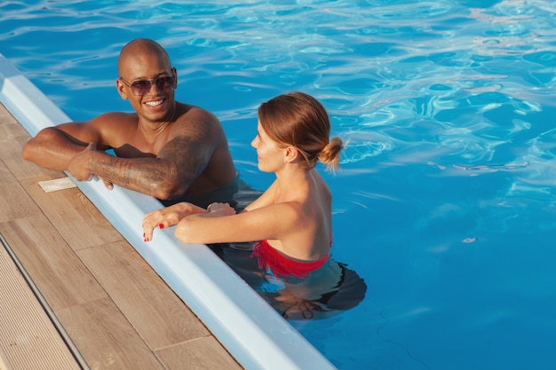 Happy multiethnic couple relaxing in the swimming pool together, copy space. Attractive African man and his girlfriend enjoying summer vacation at seaside resort