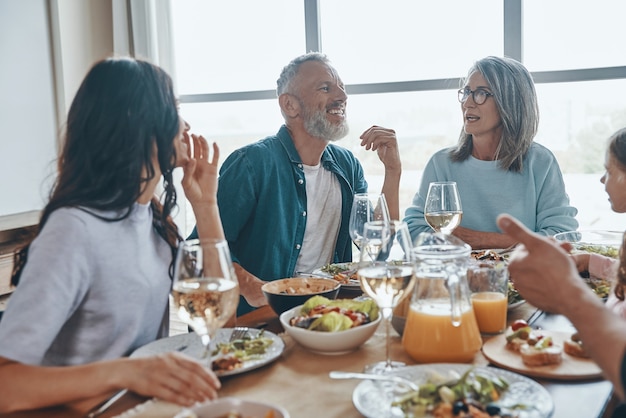 Felice famiglia multigenerazionale che comunica e sorride mentre cena insieme