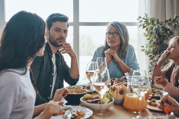 Felice famiglia multigenerazionale che comunica e sorride mentre cena insieme