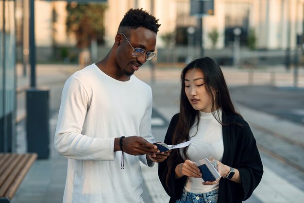 Happy multiracial couple look at boarding pass checking departure time at the stop near airport. Vacations trip concept.