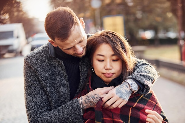 Happy multiracial couple warming up by red plaid together outdoors in the city.