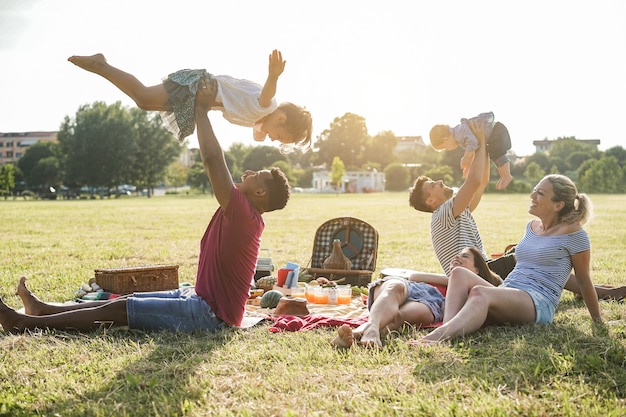 Happy multiracial families doing picnic outdoor in city park during summer vacation - Main focus on right woman face