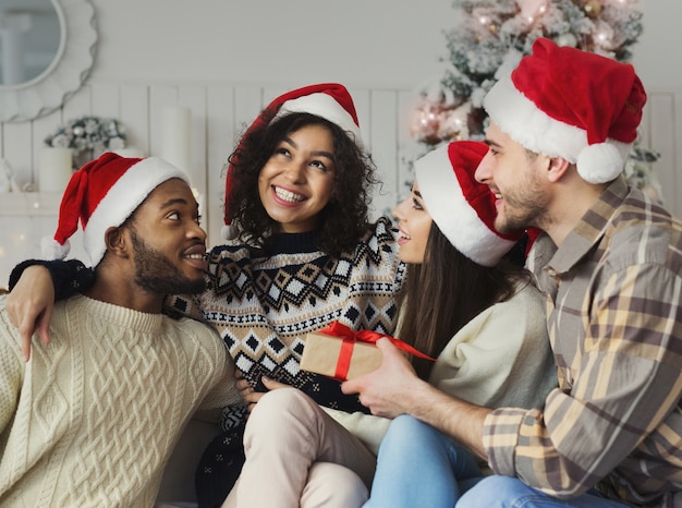 Happy multiracial friends exchanging gifts and having fun near new year tree