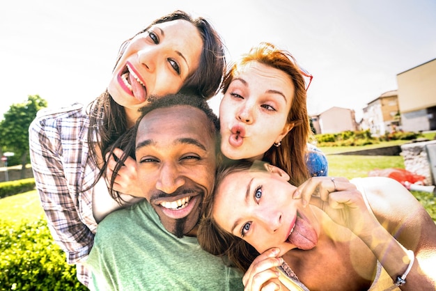 Happy multiracial friends group taking selfie sticking tongue\
out with funny faces young people sharing stories on social network\
community millennials lifestyle concept on vivid vintage\
filter