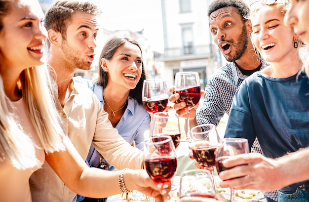 Happy multiracial friends having fun drinking and toasting red wine at lunch party