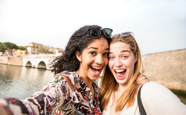 Happy multiracial girlfriends taking selfie and having fun outddors