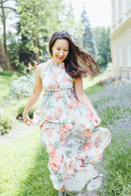 Happy multiracial Japanese woman in romantic floral maxi dress in summer park