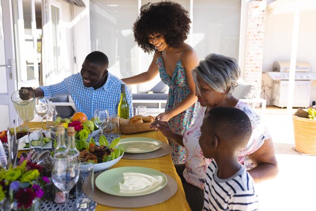 Photo happy multiracial woman with afro hair serving bread to multigeneration family at dining table. home, lunch, food, drink, unaltered, togetherness, love, childhood, lifestyle and retirement concept.