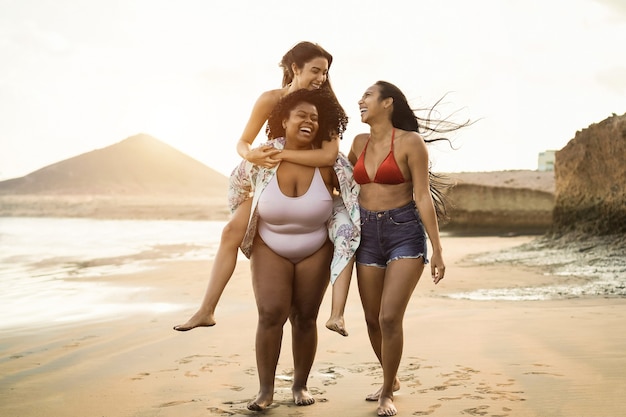 Happy multiracial women with different bodies and skins having\
fun in summer day on the beach - focus on african girl face