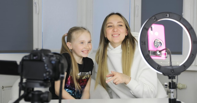 Foto la mamma felice e la figlia carina del bambino ridono usano lo smartphone. madre con bambino prende selfie guarda i cartoni animati fare videochiamata sul cellulare seduto a casa.