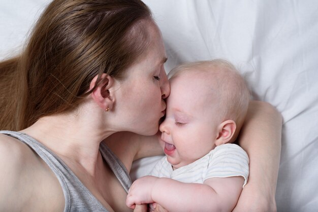 幼児の子供を手に持って幸せなお母さん。彼女の赤ちゃんにキスする美しい若い母親。