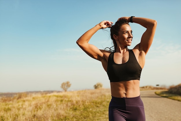 Happy muscular build woman tying up her hair while running in nature Copy space