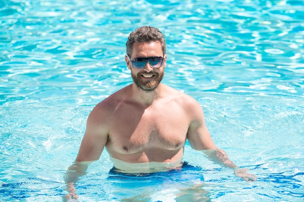 Happy muscular man in glasses swimming in pool on summer summertime