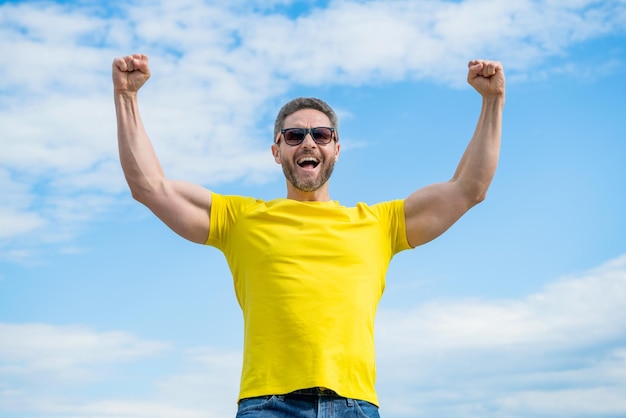 Happy muscular man in yellow shirt and sunglasses on sky background