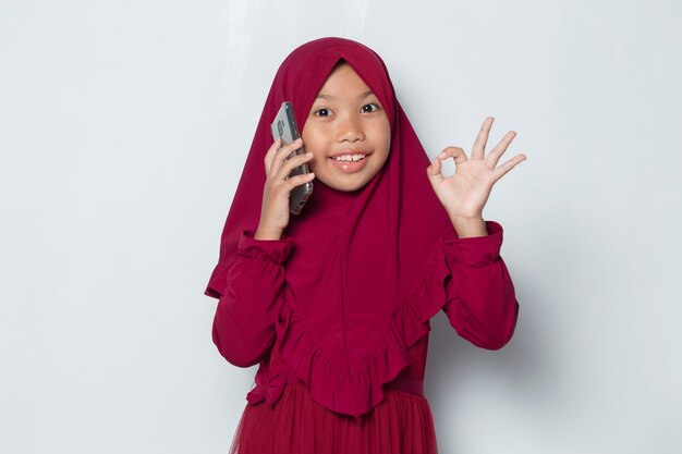 白い背景の上のスマートフォンを使用して幸せなイスラム教徒のアジアの少女