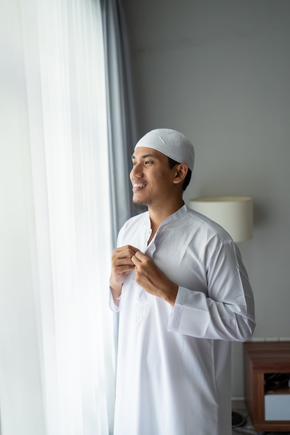 Happy muslim asian man standing near window get dressed before going to the mosque