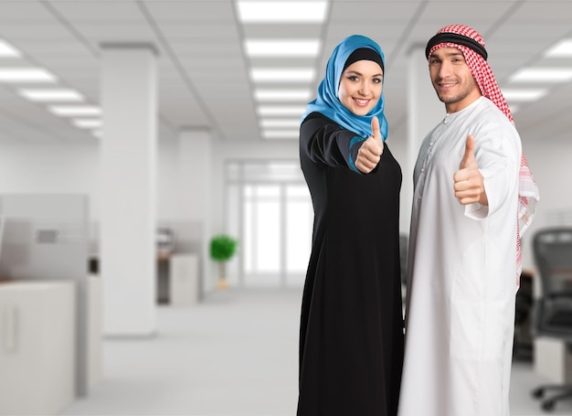 Счастливая мусульманская пара улыбается, показывая большие пальцы на светлом фоне