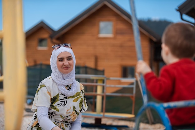 A happy Muslim family is having fun in the park mother in a hijab pushes the child's son on a swing