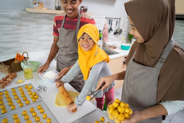 Felice famiglia musulmana con l'hijab che prepara la torta nastar insieme a casa. bella attività di cucina per genitori e figli per eid mubarak