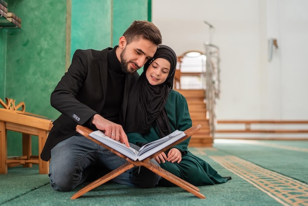 A happy Muslim family young father with child daughter reading a Quran inside the Mosque