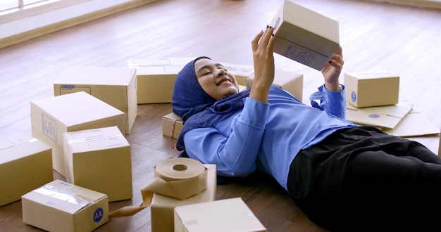 Счастливая мусульманская женщина мерчендайзера держа коробку посылки в офисе.