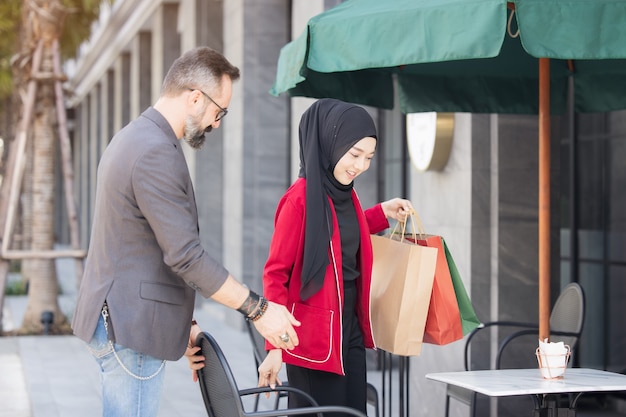 幸せなイスラム教徒の女性と少年は紙袋を持って都市の買い物の手で友達