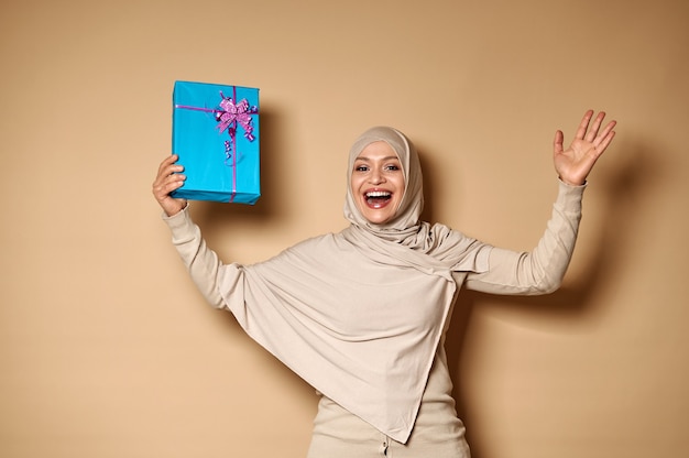행복을 표현하는 선물로 그녀의 손을 올리는 히잡의 행복한 무슬림 여성