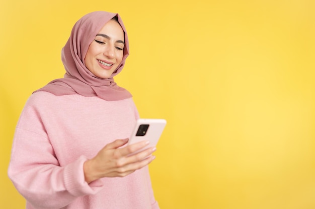 Счастливая мусульманка улыбается, используя мобильный телефон