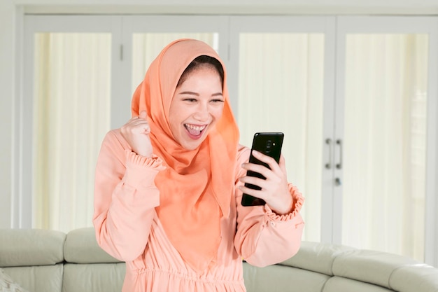 Happy Muslim woman using a phone at home