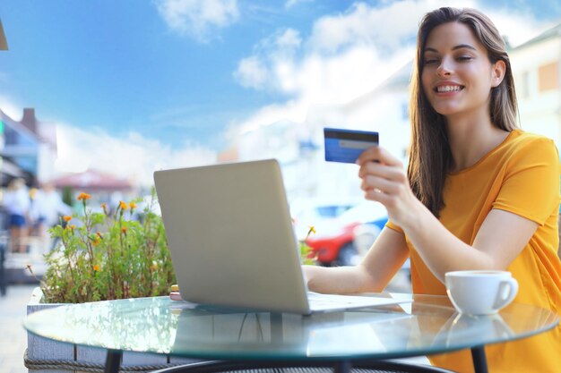 Happy natural brunette using credit card and laptop in cafe outdoors