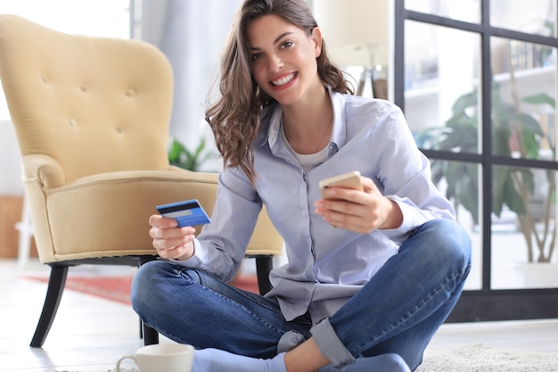 Happy natural brunette using credit card and mobile phone in the living room.