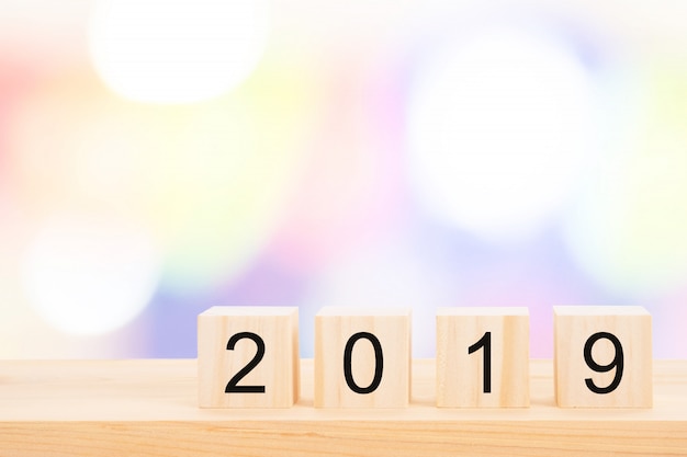 Happy new year 2019 text on wooden cubes on wooden pine table and blur light bokeh.