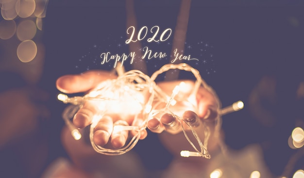 Happy new year 2020 glowing word over hand with party light string bokeh