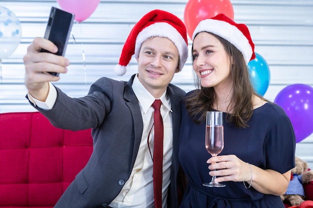 Happy new year 2022 concept, Selfie of Happy couple holding the champagne glass in Christmas and New Year's Eve party Christmas tree background After finishing business work