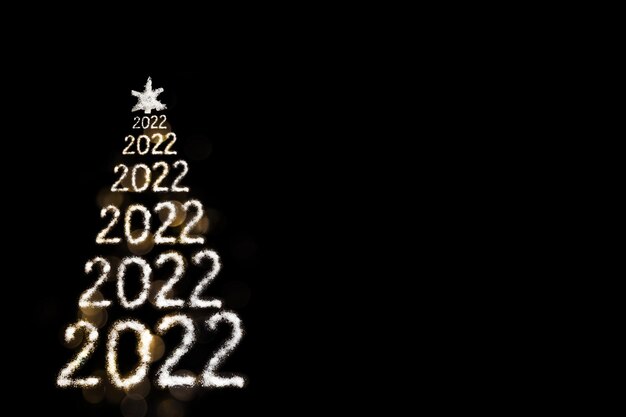 写真 明けましておめでとうございます2022年。2022年からの創造的な雪に覆われたクリスマスツリーとボケ味で黒い背景に分離された星。雪のような海塩で作った手作りのクリスマスツリー。