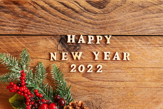 Happy New Year 2022. Quote made wooden letters and 2022 on wooden background  fir tree branch cones.