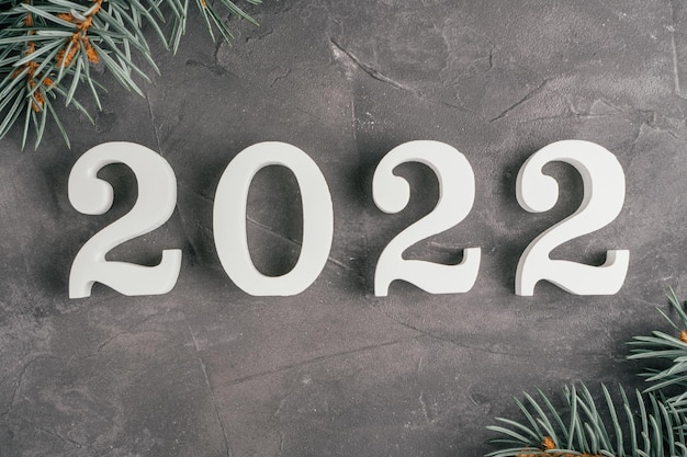 Happy New Year 2022. White numbers 2022 lying on gray uneven concrete surface with Christmas tree branches. Top view