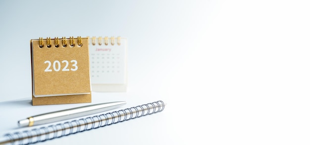 Happy new year 2023 banner background 2023 numbers year on\
small beige desk calendar cover on notepad with pen on white\
background with copy space to do list concept