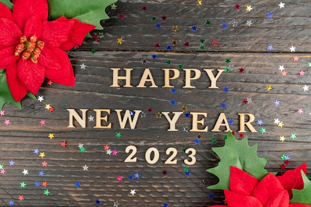 Photo happy new year 2023 celebration wooden text and poinsettia on wooden background flat lay