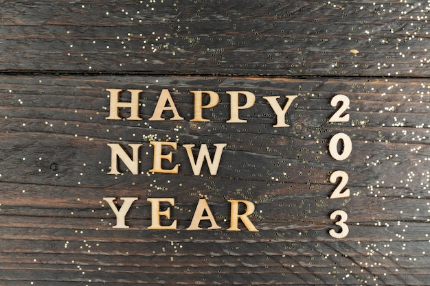 Photo happy new year 2023 celebration wooden text on wooden background with scattered golden confetti