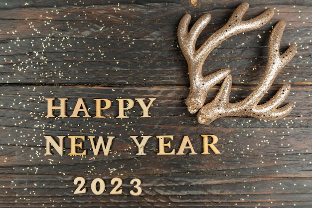 Happy new year 2023 quote made of wooden letters and golden reindeer horns as decoration Festive greeting card wor christmas and new year holidays