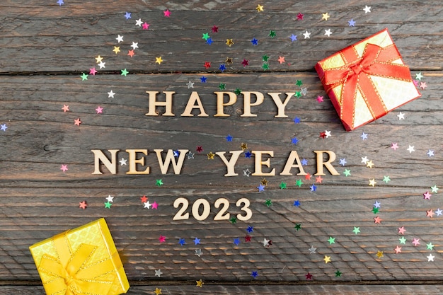 Happy new year 2023 next and red and yellow small gift boxes on dark wooden background with confetti