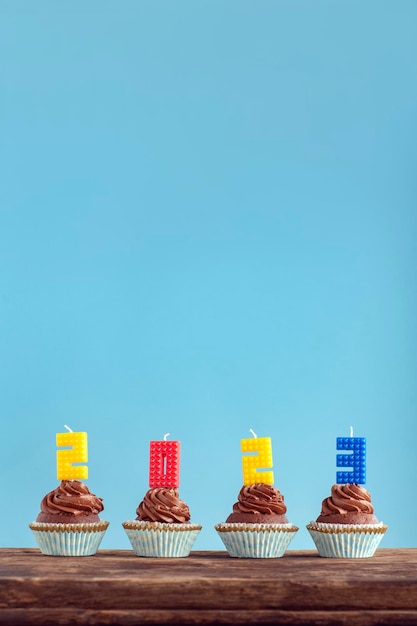 Photo happy new year 2023 theme homemade chocolate cupcakes with 2023 number colorful candle on wooden table vertical frame blue background