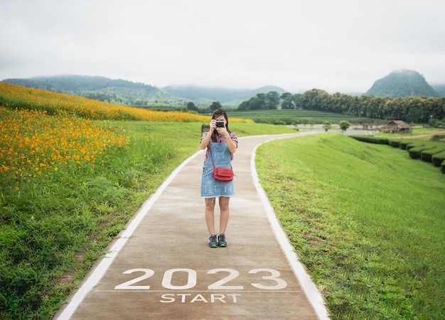 明けましておめでとうございます 20232023 は、新年の始まりを象徴しています 自然の新鮮な緑茶と花の農場の山の壁紙の道で旅行者の女性の写真撮影に手紙が新年2023を開始します